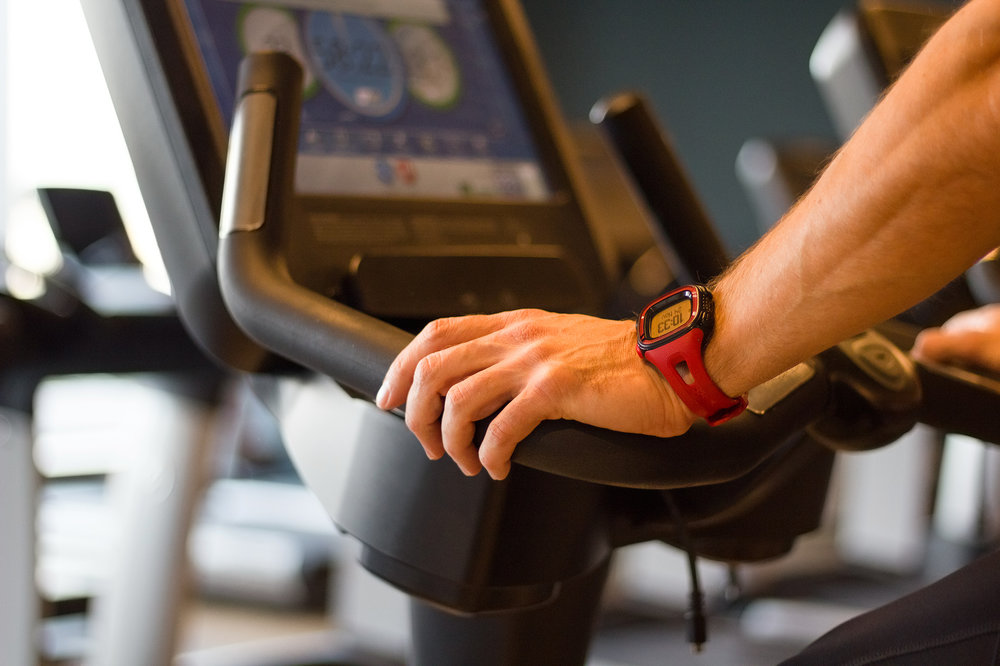 Athletic man cycling on stationary bike in gym. Focus on his hand on the handlebar.